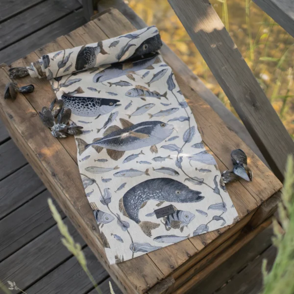 Beige och blå bordslöpare i 100 % linne med fiskar som mönster, tillverkad av NORDRÅ Sweden som säljer presenter och inredning.