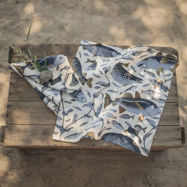 Beige och blå servetter i 100 % linne med fiskar som mönster, tillverkad av NORDRÅ Sweden som säljer presenter och inredning.