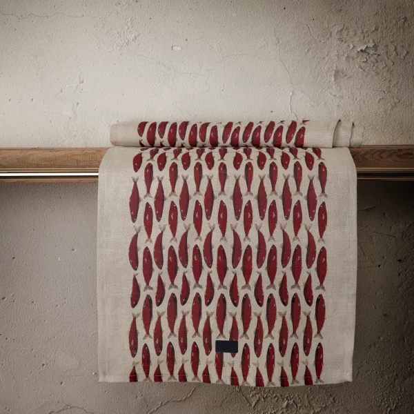 Röd och beige bordslöpare i linne med fiskar som mönster, tillverkad av NORDRÅ Sweden som säljer presenter och inredning.