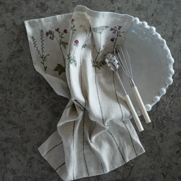 Beige kökshandduk i 100 % linne med blommor som mönster, tillverkad av NORDRÅ Sweden som säljer presenter och inredning.